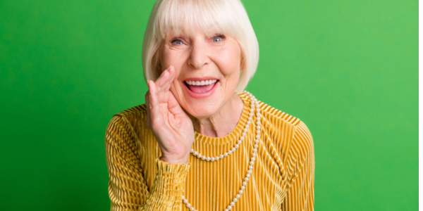 Senior Woman in Orange Shirt with Green Background makes whispering motion