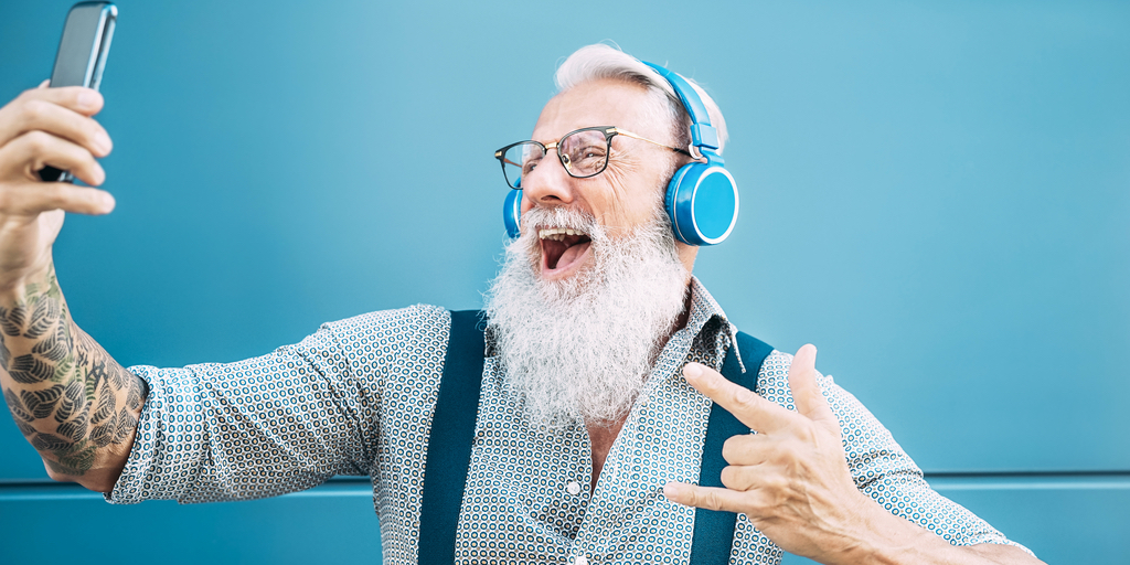 Senior man laughing at his phone while wearing headphones
