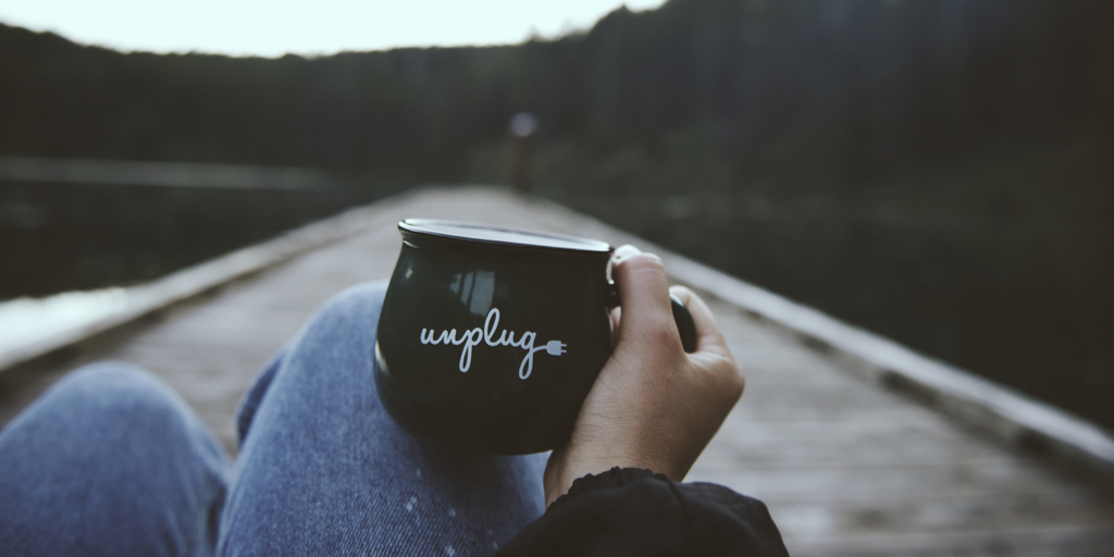 First-person perspective of someone holding a coffee mug on a lack dock that says "unplug"