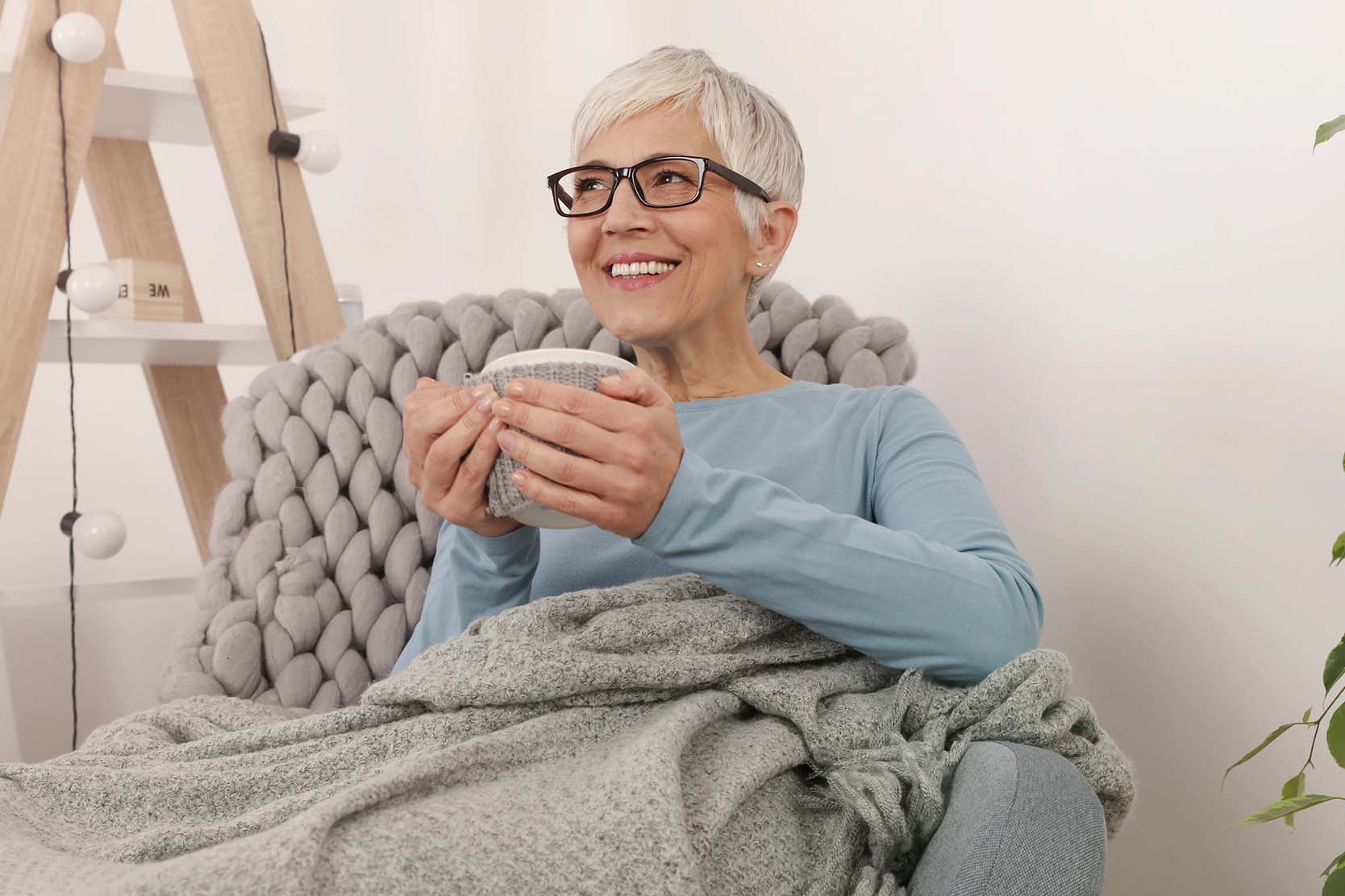 Senior woman enjoys a hot cup of tea in a comfy chair and blanket